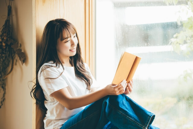 雨の日、窓際に座って読書をする女性