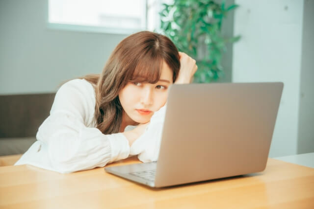 勉強に疲れてパソコンの前で座り続ける若い女性