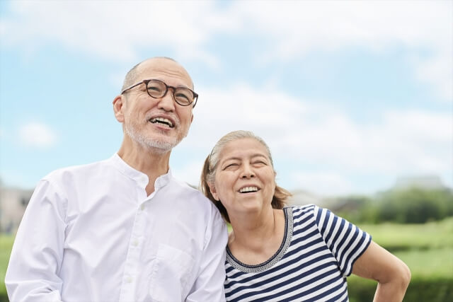 青空を背景に笑顔で立つ高齢者の夫婦