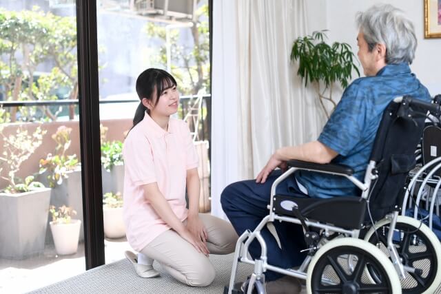 車椅子に乗る高齢者と会話をする理学療法士