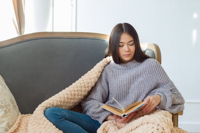 つらいときにソファーで本を読む女性