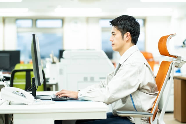 パソコン作業をする作業着を着た男性