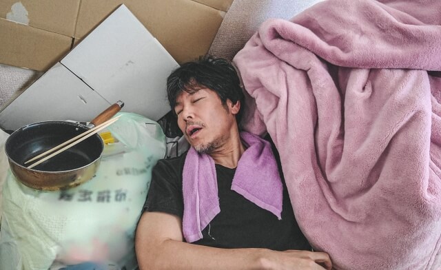 ゴミ部屋で寝る疲れた顔の中年男性
