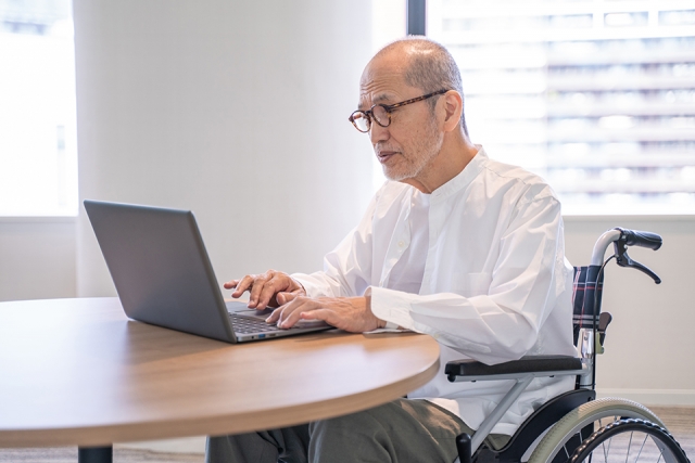 パソコン作業をするシニア車椅子に乗る男性